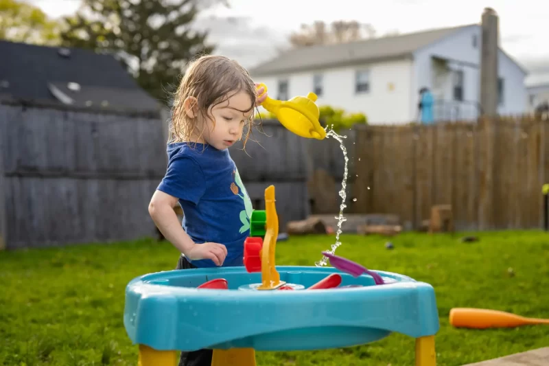 A young toddler enjoying her water table in a backyard on a summer day