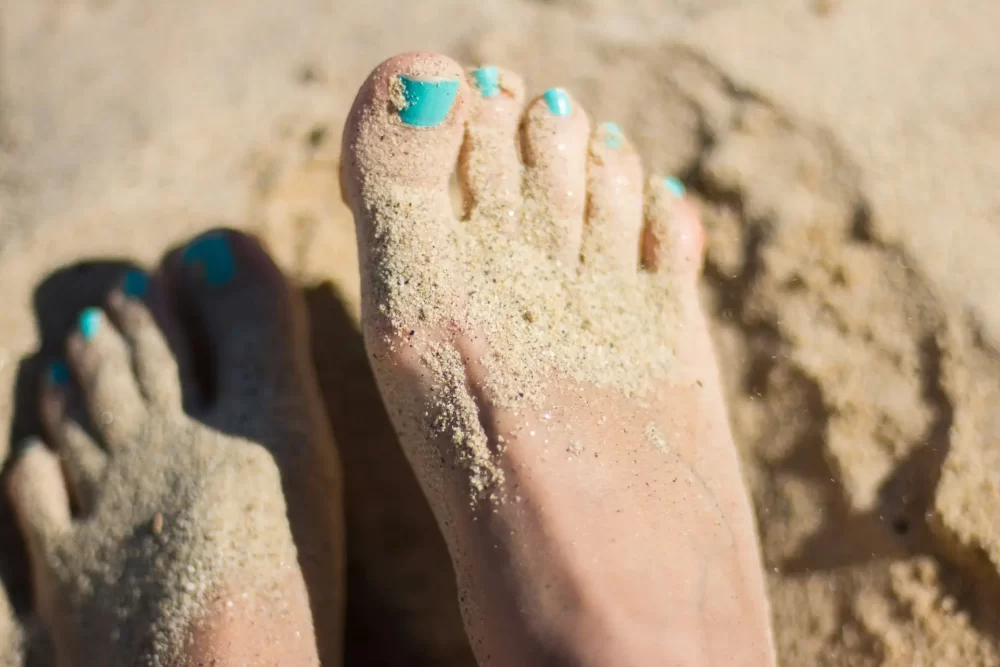 Toes painted baby blue on a woman sitting in the sand on a beach