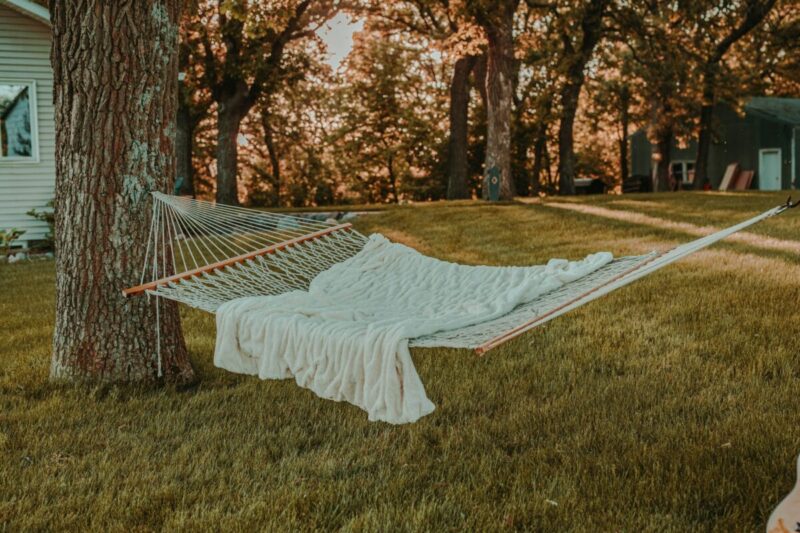 A beautiful white woven hammock hanging between two trees in a backyard