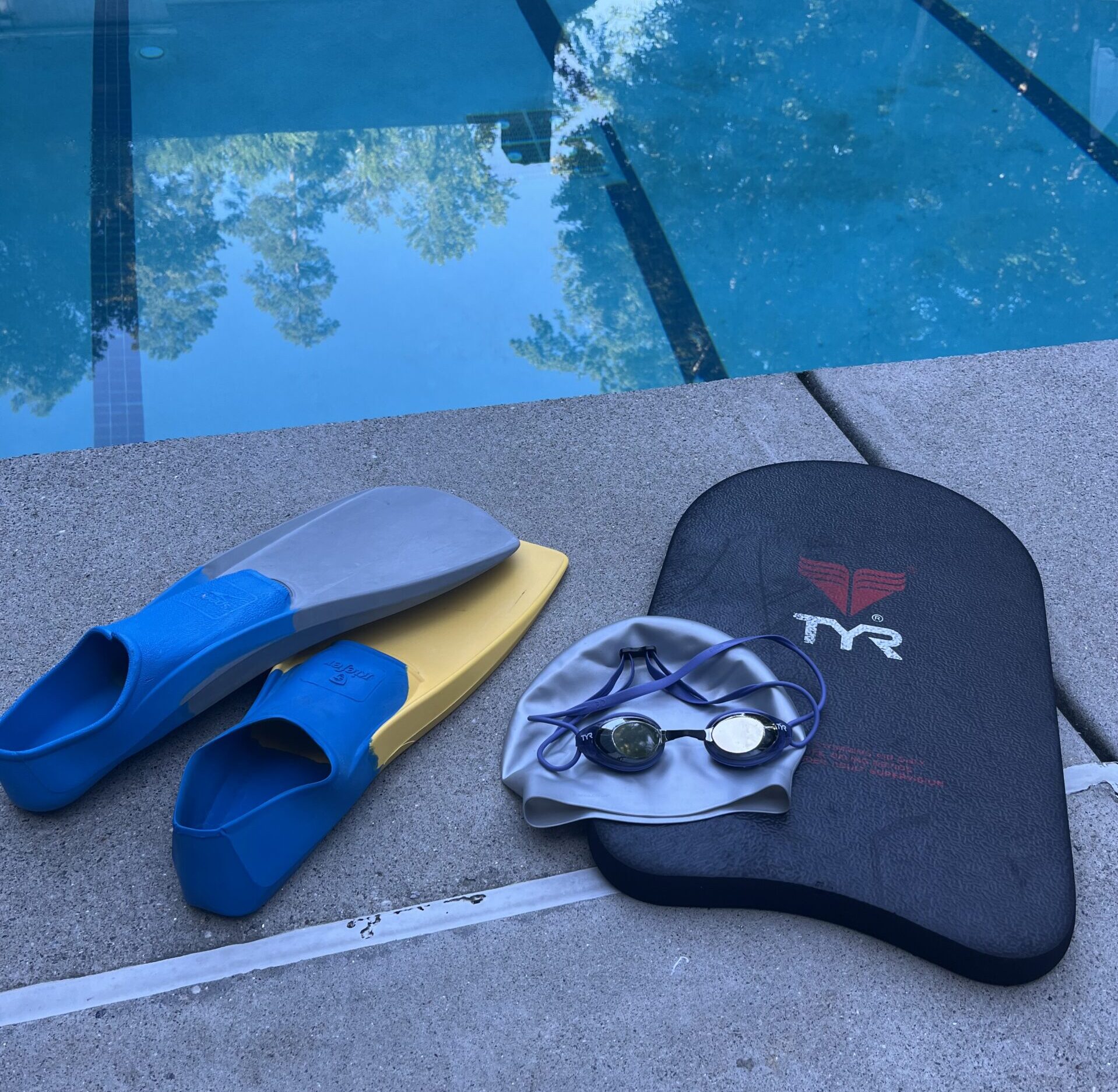 Swim gear on side of pool to use for a swim workout including goggles, swim Finn's, kickboard