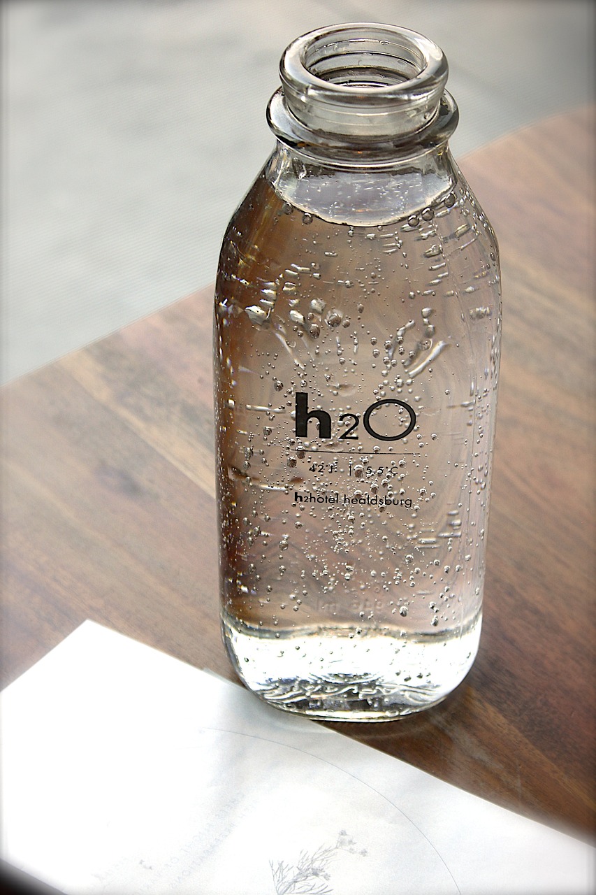Glass bottle that says H20 filled with water sitting on small table by pool