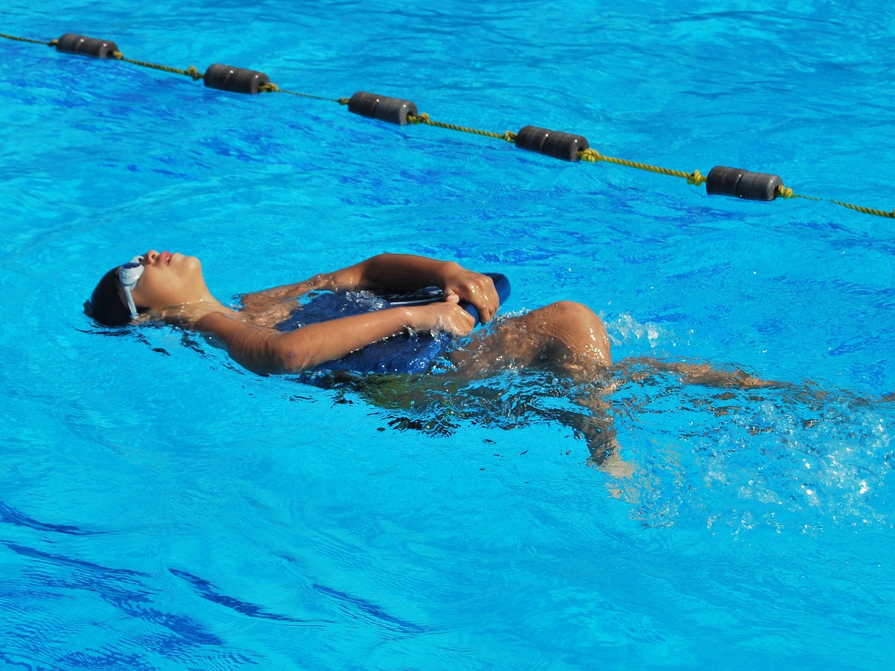 child learning how to swim in pool back float using kickboard