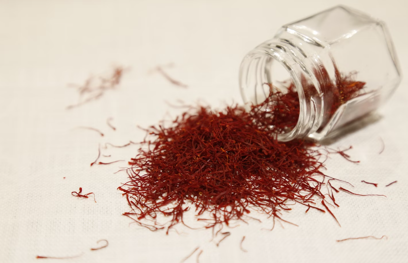 Saffron spice spilling from glass jar on white table