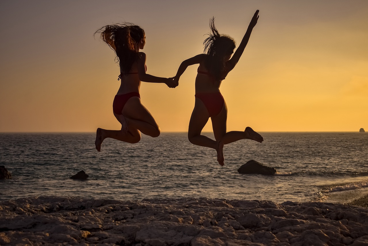 girls jumping together on beach during sunset